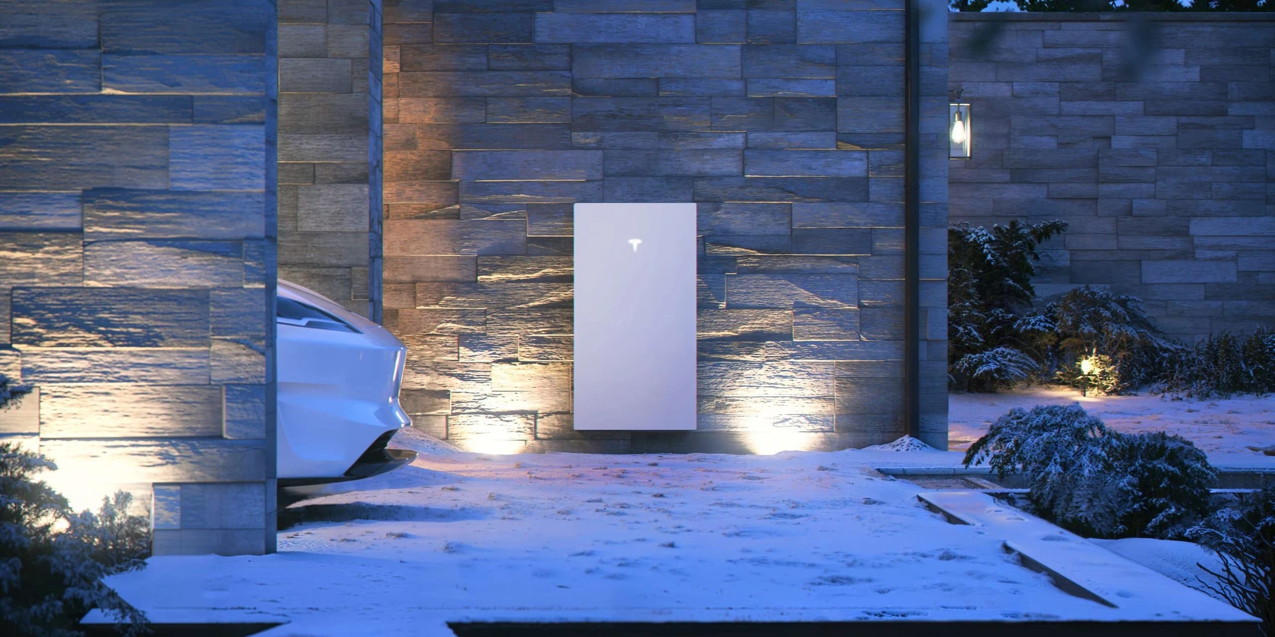 De Tesla Powerwall aangelicht aan een stenen muur in een besneeuwde tuin